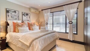 Een slaapkamer met een groot bed, twee wandairconditioners en een raam met zonwering en gordijnen.