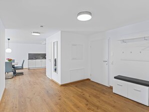 Ein moderner, gut beleuchteter Raum mit Holzboden, weißen Wänden, einem Essbereich mit Tisch und Stühlen sowie einer Küchenzeile.