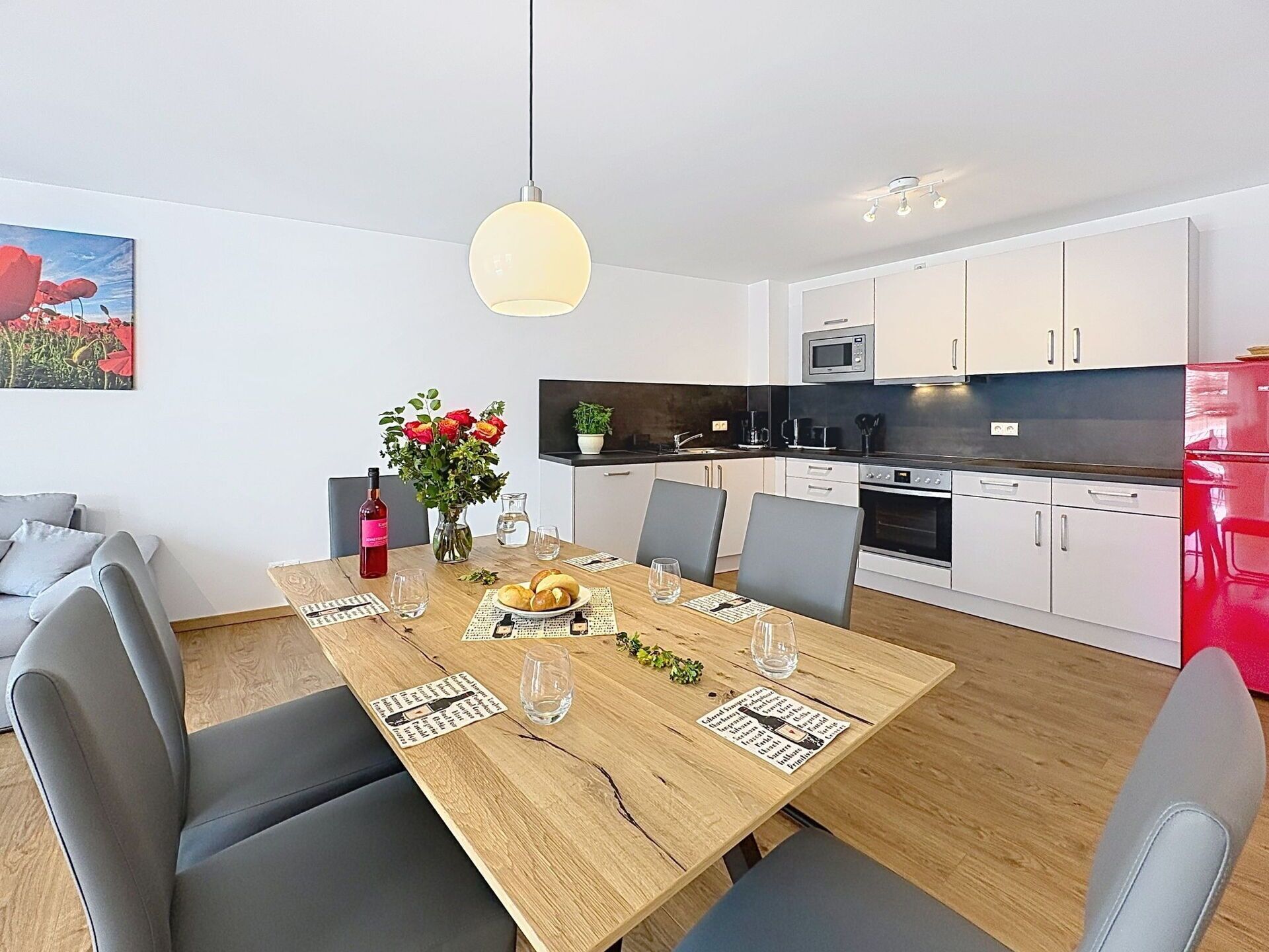 A modern kitchen with white cabinets, a red refrigerator, and a dining area with a wooden table set for two.