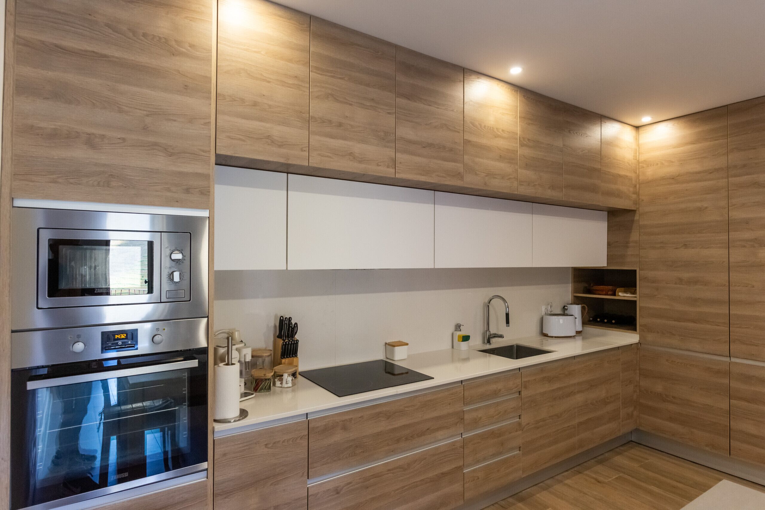Una cocina moderna con armarios de madera, electrodomésticos de acero inoxidable, encimera negra y un lavamanos empotrado.
