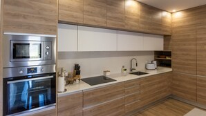 A modern kitchen with wooden cabinetry, stainless steel appliances, a black countertop, and a built-in sink.