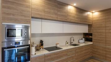 Una cocina moderna con armarios de madera, electrodomésticos de acero inoxidable, encimera negra y un lavamanos empotrado.