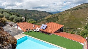 A pool with a red-roofed building, a green lawn, and a mountainous landscape in the background.