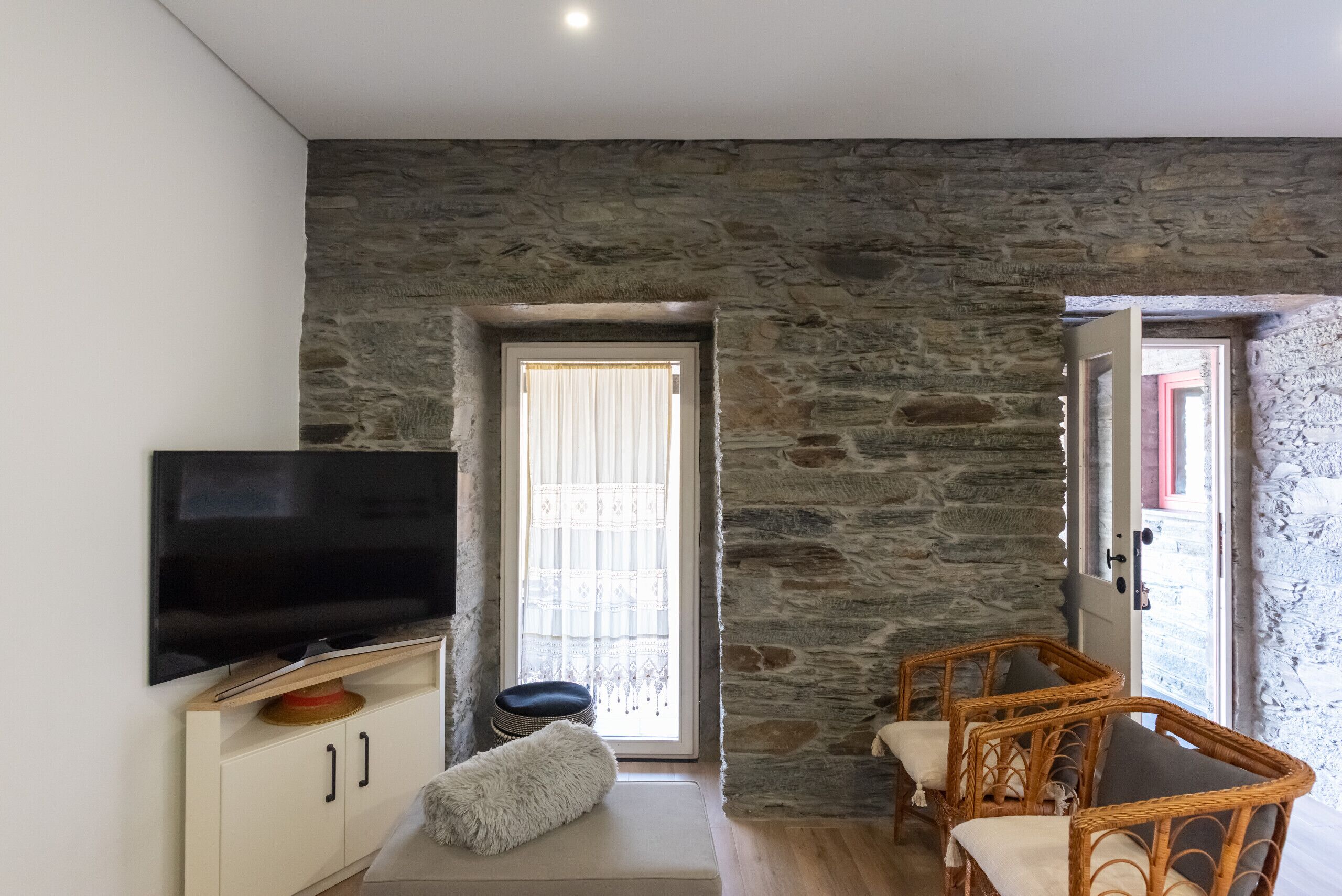 Una habitación con pared de piedra, televisor sobre un mueble, un sofá y sillones de mimbre.