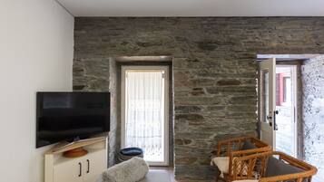 Una habitación con pared de piedra, televisor sobre un mueble, un sofá y sillones de mimbre.