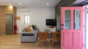 A modern living room with a grey sofa, a television, wicker chairs, and a pink door.