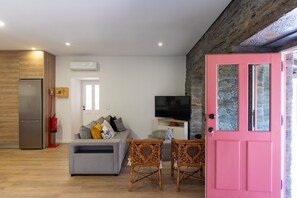 A modern living room with a grey sofa, a television, wicker chairs, and a pink door. - Feel Discovery Casa Fonte do Lagar (Desejosa)