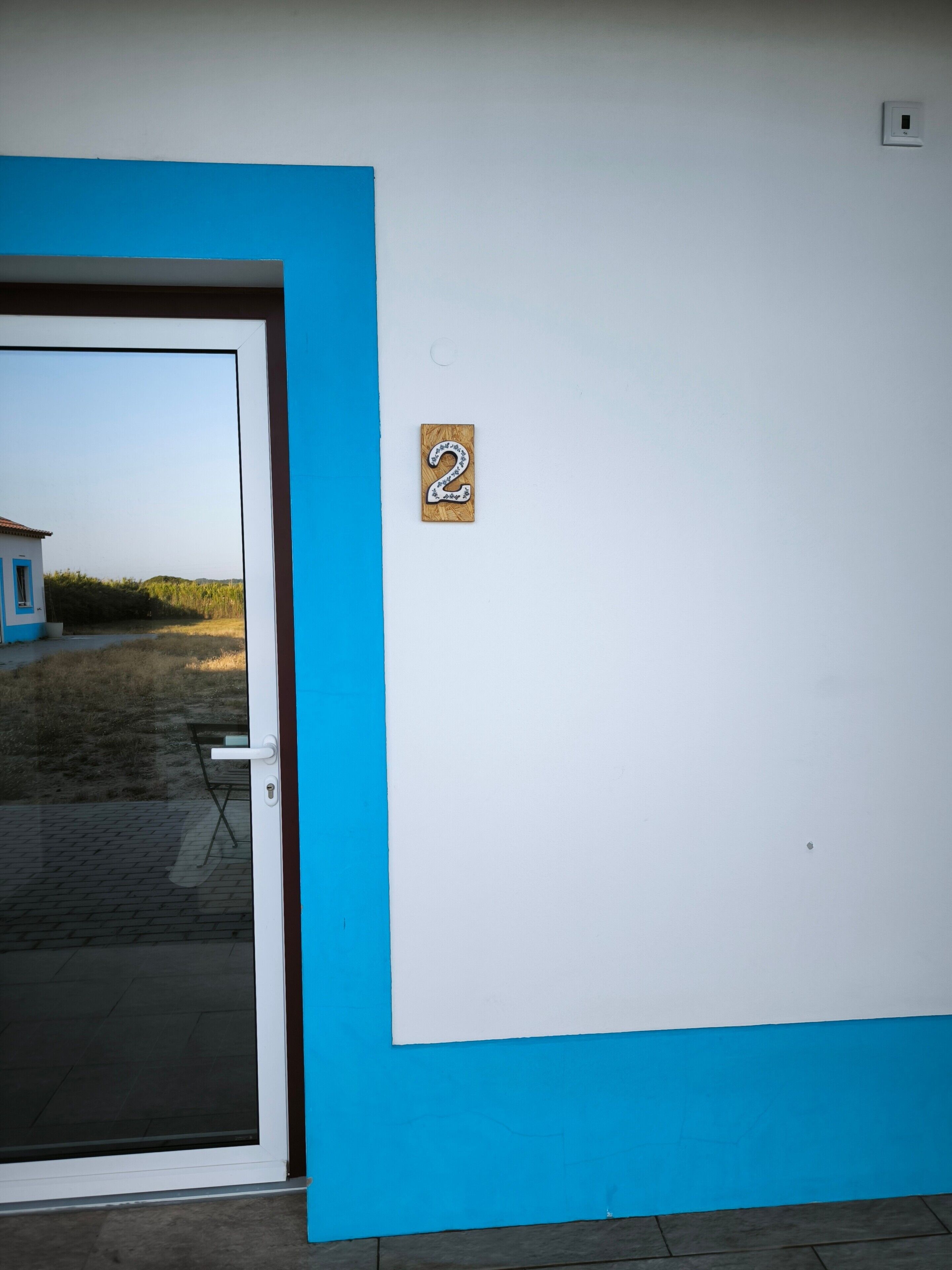 Una stanza con una parete blu e bianca, una porta con un pannello in vetro e un piccolo cartello con un numero sulla parete.
