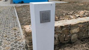 Une boîte électrique blanche dotée d’un clavier, un mur en pierre et une zone pavée avec un bâtiment en arrière-plan.
