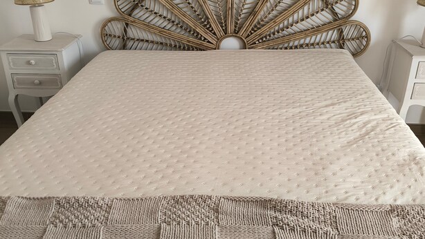 Un lit avec une tête de lit en osier, une couvre-lit à motifs et un plaid tricoté.