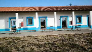 Il s’agit d’un bâtiment doté d’un toit recouvert de tuiles, de plusieurs portes et de fenêtres. On y trouve également des tables et des chaises à l’extérieur.