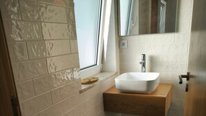 Une salle de bain avec un lavabo blanc, un plan de toilette en bois et une fenêtre.