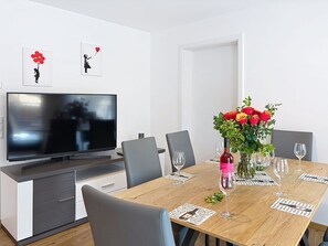 Ein moderner Essbereich mit einem Holztisch, Stühlen, einem Fernseher und einer Blumenvase.