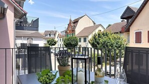 Ein Balkon mit einem Esstisch, dekoriert mit Trauben in einer Schale, einer Kerze, einer Weinflasche und einem Glas.