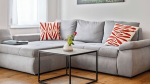 Ein modernes Wohnzimmer mit einem grauen Sofa, einem kleinen Tisch mit schwarzem Rahmen und einer Vase mit Blumen.