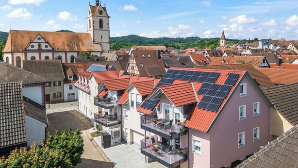 Eine Stadt mit traditioneller Architektur, darunter ein Kirchturm und Wohnhäuser mit roten Ziegeldächern.