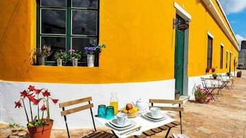 Un edificio amarillo con una ventana, una puerta y una mesa puesta con platos, tazas y una botella.
