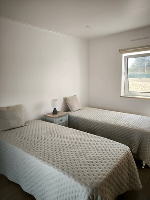 Quarto com duas camas, mesa de cabeceira, luminária e janela com vista para o exterior.