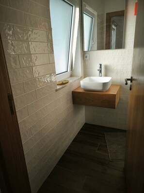 Ein Badezimmer mit einem weißen Waschbecken, einer Holzauslage und einem Fenster.