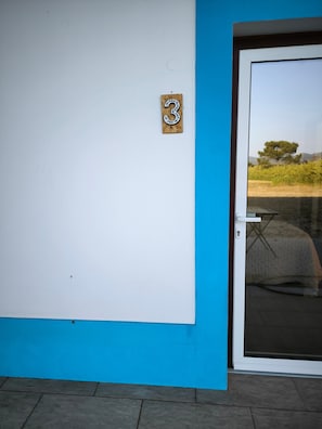 Ein Gebäude mit blau-weißer Fassade, einer Glastür und einem Schild mit der Nummer 3 an der Wand.