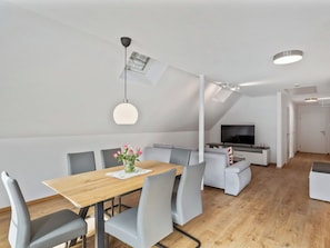 Ein moderner Wohnraum mit Essbereich, Sitzgelegenheiten, einem Fernseher und einer Treppe.