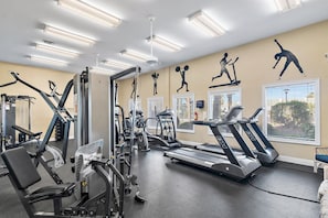 Ein Fitnessraum mit verschiedenen Trainingsgeräten, darunter Laufbänder und Kraftgeräte, sowie großen Fenstern mit Jalousien.