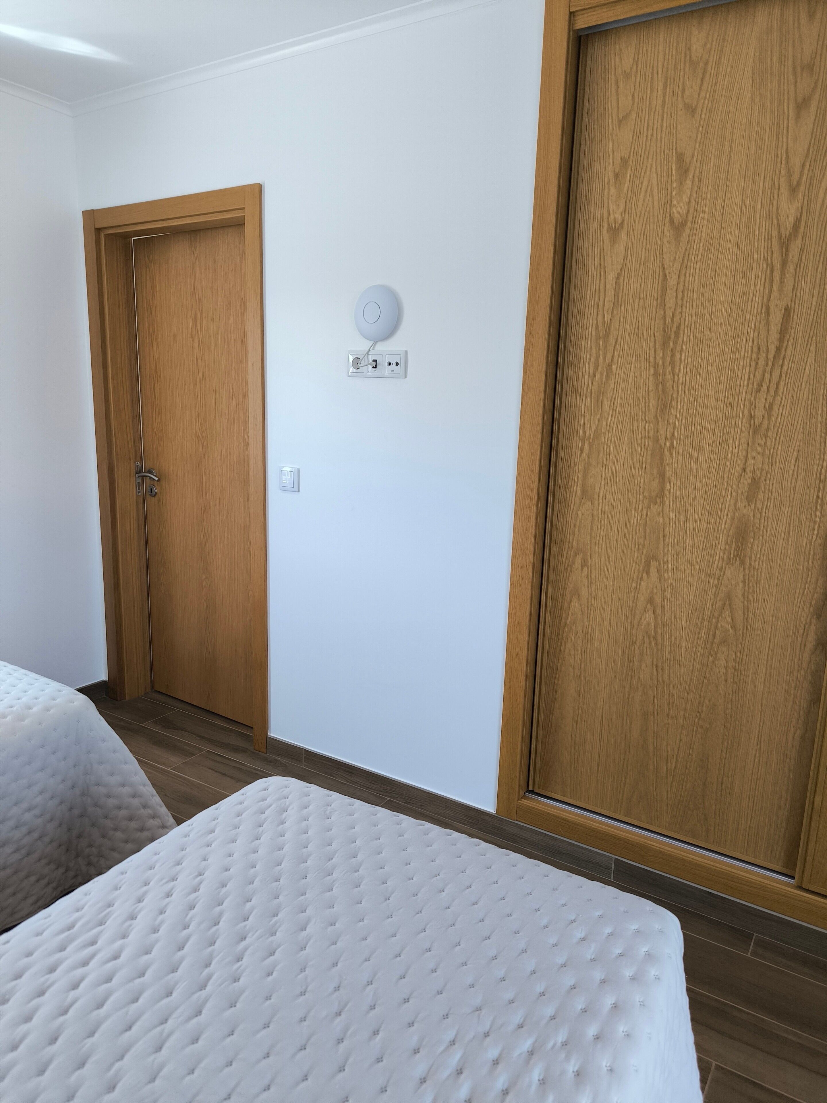 Een kamer met twee bedden, houten kasten, een stopcontact en een lichtschakelaar.