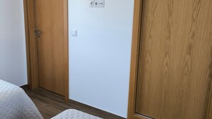 Ein Zimmer mit zwei Betten, Holzschränken, einer Steckdose und einem Lichtschalter.