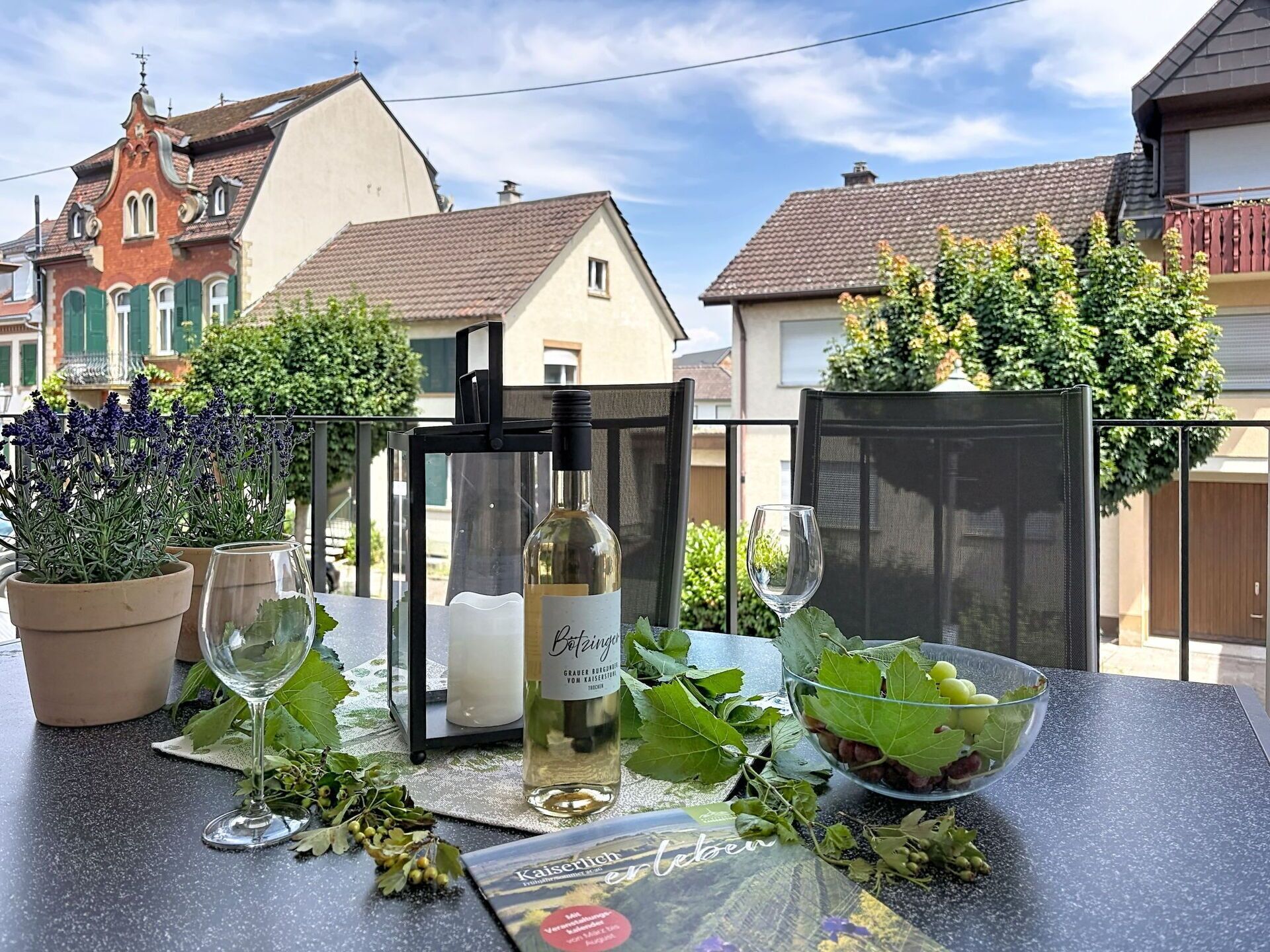 Ett bord dukat utomhus med en vinflaska, glas och en skål med druvor.