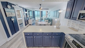 A modern kitchen with a central island, built-in cabinets, and a dining area with a round table and chairs. - Completely Renovated Luxury 1BR SunDestin 1016 w/ washer dryer (Destin)