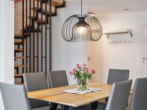 Ein Essbereich mit Holztisch, grauen Stühlen, einer Blumenvase und einer besonderen Pendelleuchte.