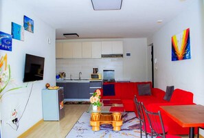 Ein gemütlicher Wohnbereich mit Küchenzeile, einem roten Sofa, einem kleinen Esstisch und einem an der Wand befestigten Fernseher.