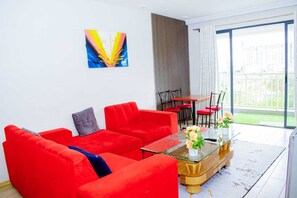 Ein modernes Wohnzimmer mit einem roten Sofa, einem Glastisch und einem Essbereich mit Tisch und Stühlen.