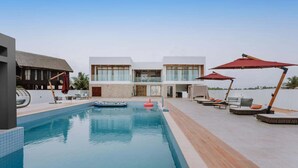 A swimming pool with lounge chairs and umbrellas, a modern building with large windows, and a clear sky.