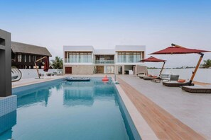 A swimming pool with lounge chairs and umbrellas, a modern building with large windows, and a clear sky.