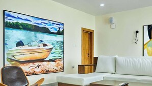 A living room with a sofa, a coffee table, a chair, and a large painting of a boat on water.