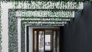 A hallway with a modern design, featuring a glass door with a leaf pattern, a tiled floor, and a dark wall on one side.