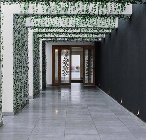 A hallway with a modern design, featuring a glass door with a leaf pattern, a tiled floor, and a dark wall on one side.