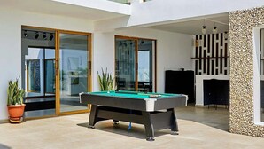 A modern multi-level house with a pool table, glass doors, and a stone wall.