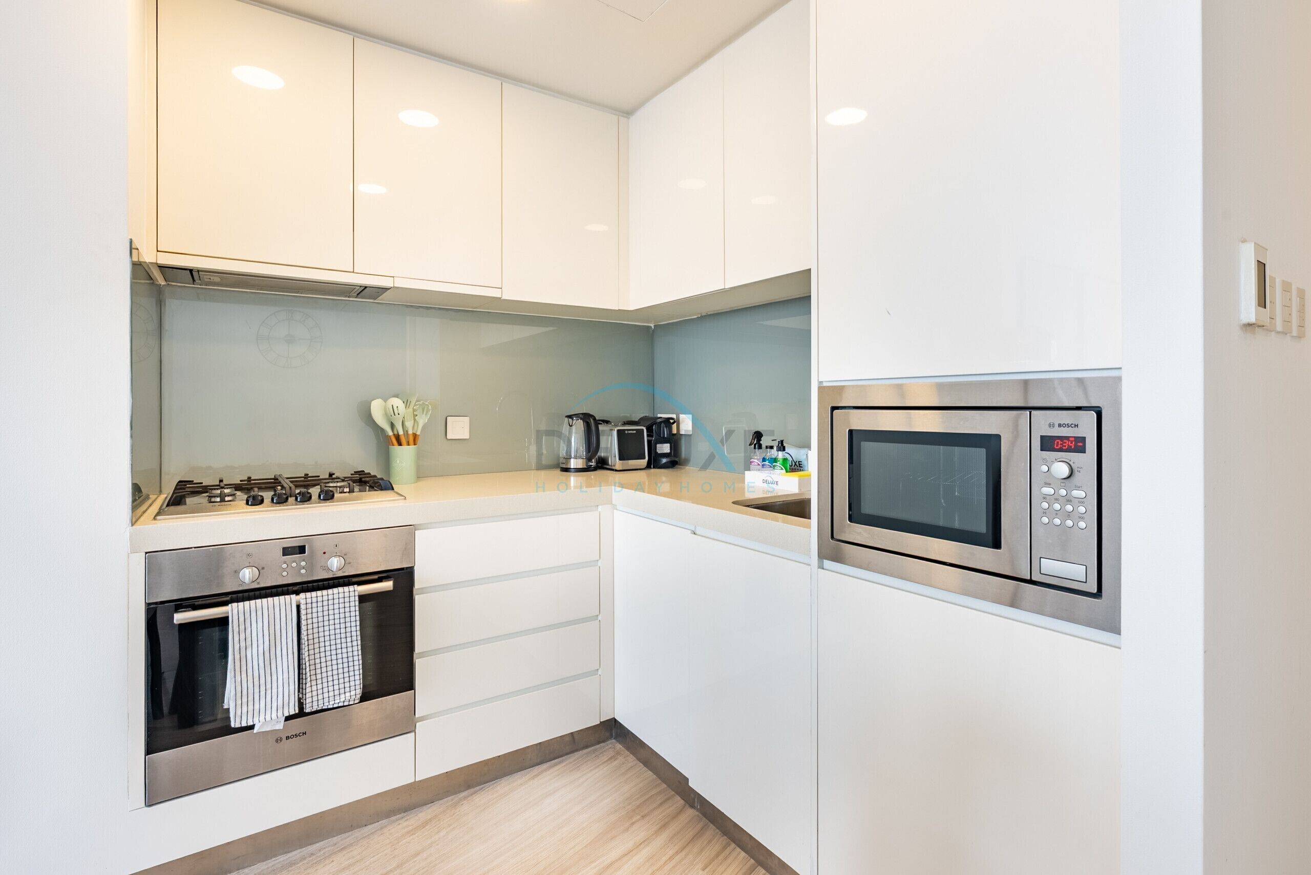 Een moderne keuken met witte kastjes, een Bosch oven, een magnetron en een koffiezetapparaat.