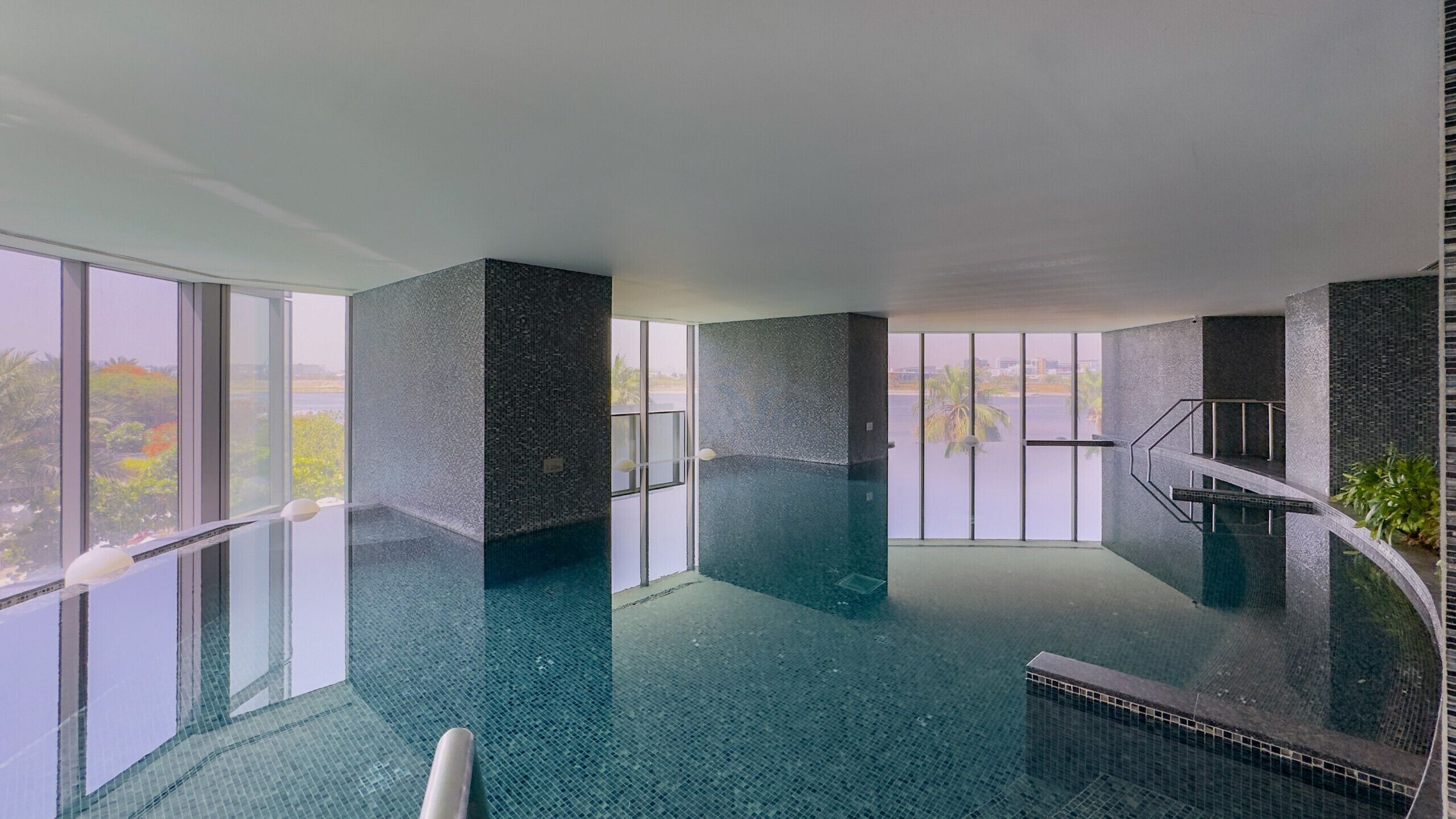 Une piscine intérieure moderne dotée d’un plancher en verre, de grandes fenêtres et offrant une vue sur le paysage urbain.