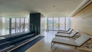 A modern indoor area with a staircase, lounge chairs, and large windows offering a view of buildings and palm trees. - Prime Creekside 1BR on the Top Floor with Harbour Views (Dubai)