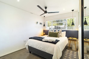 A modern hotel room with a bed, ceiling fan, bedside tables, and a window with a view.