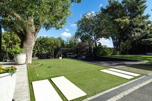 Ein gepflegter Rasen mit Putting-Grün, einem gepflasterten Weg und einem großen Baum, der Schatten spendet.