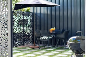 An outdoor patio with a grill, chairs, and a table with fruit.