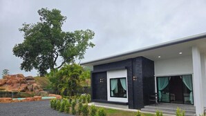 Ein modernes Gebäude mit einem großen Baum, einer Terrasse und Blick auf eine natürliche Landschaft.
