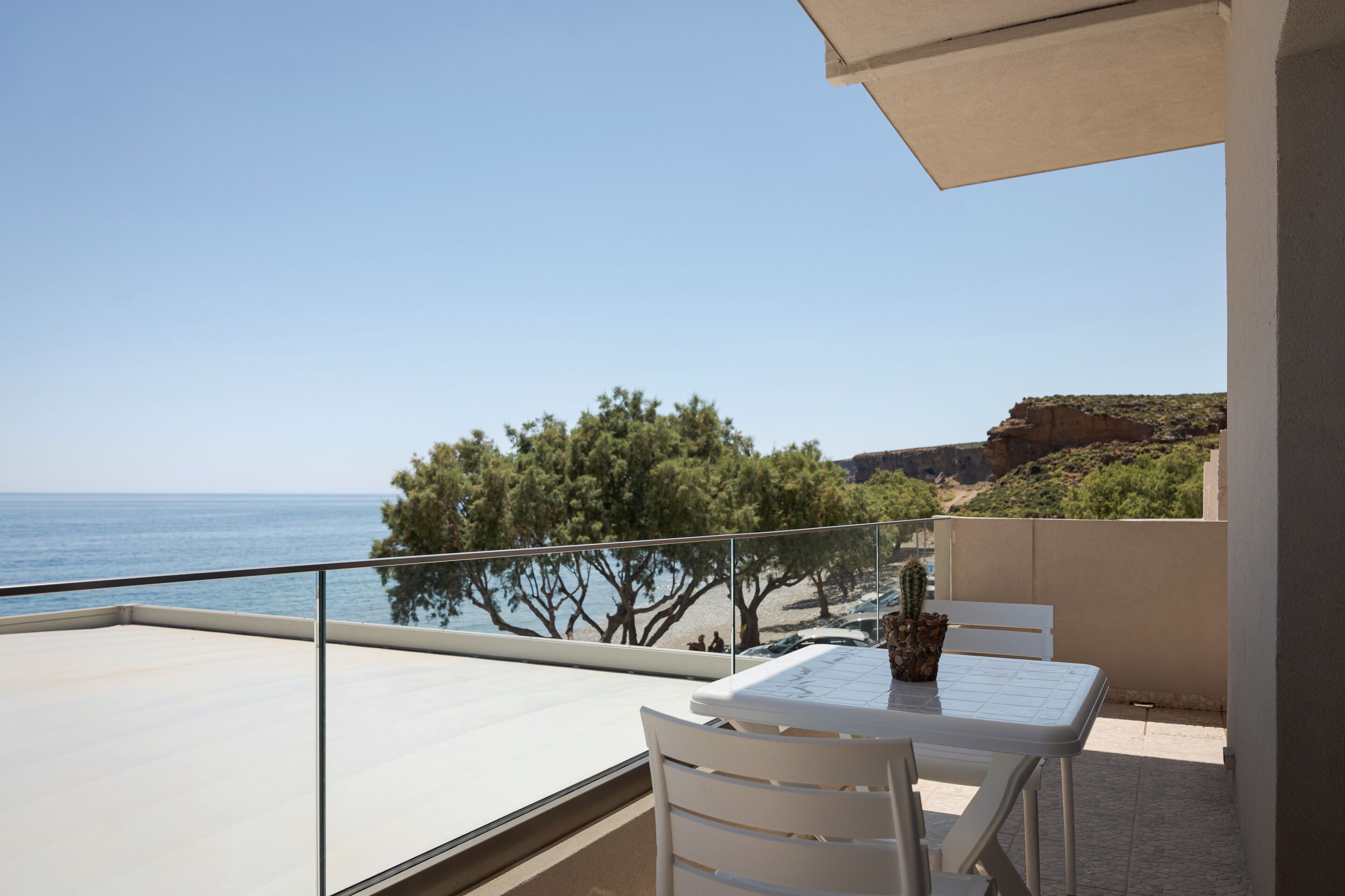 A balcony with a table and chairs, overlooking a beach and the sea.
