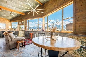 Une pièce spacieuse avec une grande table à manger en bois, un canapé et une vue sur les montagnes grâce à de grandes fenêtres.