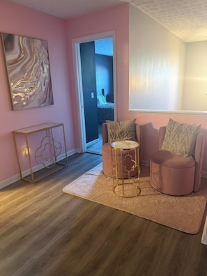 Ein Wohnzimmer mit rosa Wand, einer Marmorbildarbeit, einem runden Tisch, einer Couch und einem gemusterten Teppich.
