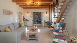 Ein modernes Wohnzimmer mit Holzbalkendecke, einer Couch, einem Couchtisch, einem gemusterten Sessel und einer Treppe.